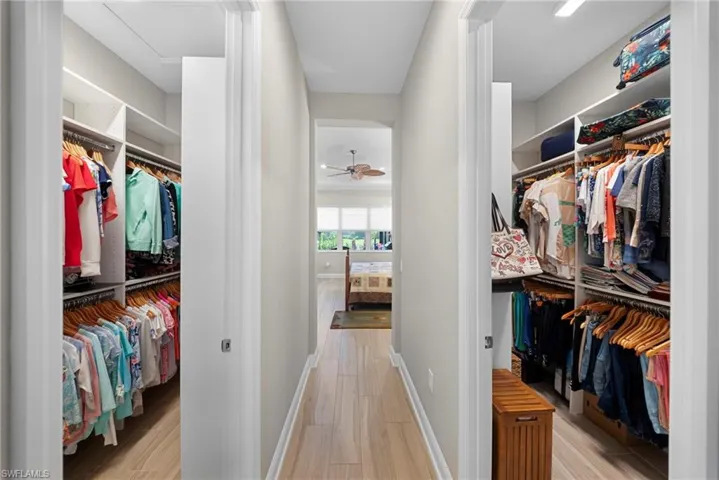 This property features extensive custom closet systems with built-in shelving and hanging rods on both sides of a hallway, leading to a room with large windows