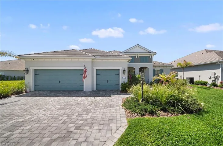 The property features a paver driveway, an attached two-car garage with light blue doors, and a well-maintained lawn with mature landscaping