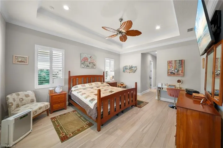 This room features light-colored flooring, a tray ceiling with recessed lighting, and a ceiling fan