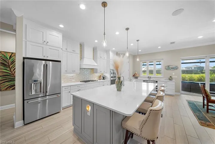 The kitchen features a large center island with seating, white shaker-style cabinetry, and a stainless steel refrigerator