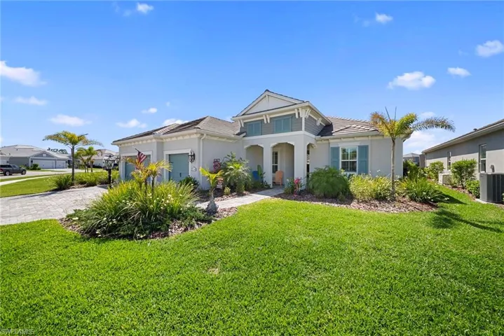 The property features a well-maintained lawn, a paved driveway, and landscaping with various plants and small palm trees