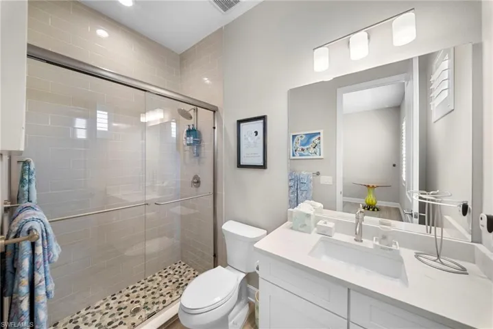 This bathroom features a contemporary vanity with a white countertop and an integrated sink, illuminated by a three-light fixture above the mirror