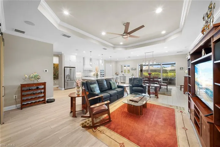 The open concept living area features a tray ceiling with recessed lighting and a ceiling fan, light-colored flooring, and a sliding glass door leading to an outdoor space