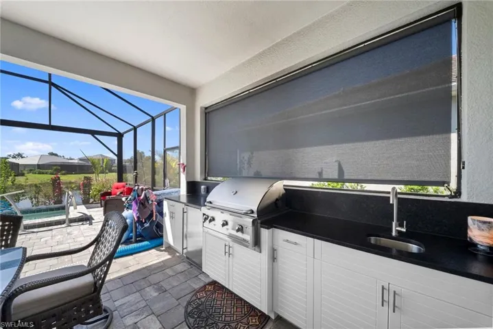 This outdoor living area features an integrated kitchen with a built-in grill, sink, and dark countertops