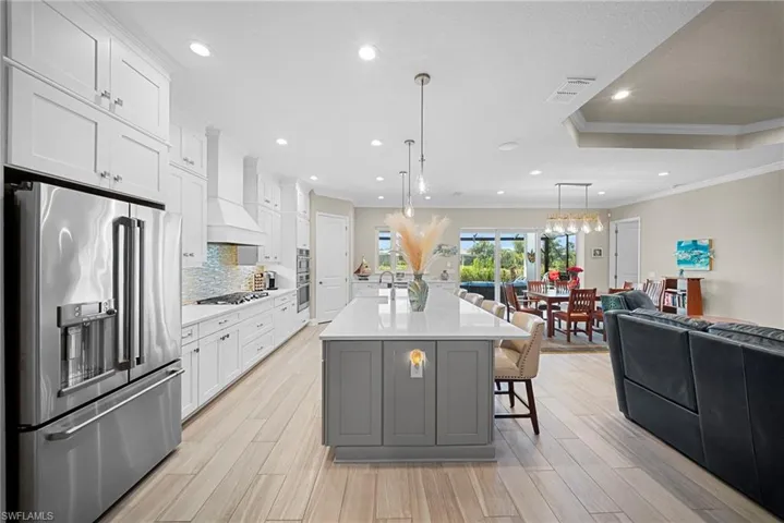This open-concept kitchen features a large center island with pendant lighting, a stainless steel refrigerator, and ample white cabinetry, complemented by light-colored flooring