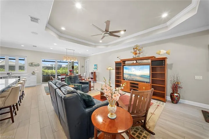 This spacious living area features light-toned flooring, a tray ceiling with recessed lighting, and a ceiling fan