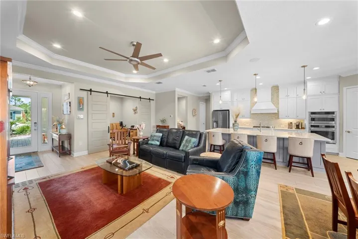 Spacious open concept living area featuring a tray ceiling with recessed lighting and a ceiling fan, light-toned flooring, and a kitchen with white cabinetry, a large island, and stainless steel appliances