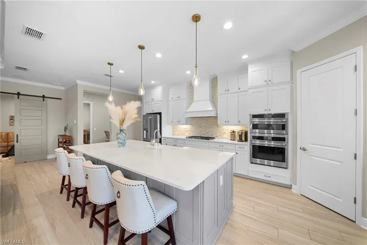 The kitchen features light wood flooring, a large island with a light-colored countertop, white cabinetry, and stainless steel appliances