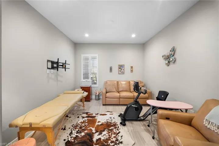 This versatile room features light-colored walls, recessed lighting, and a window with white louvered shutters, providing natural light