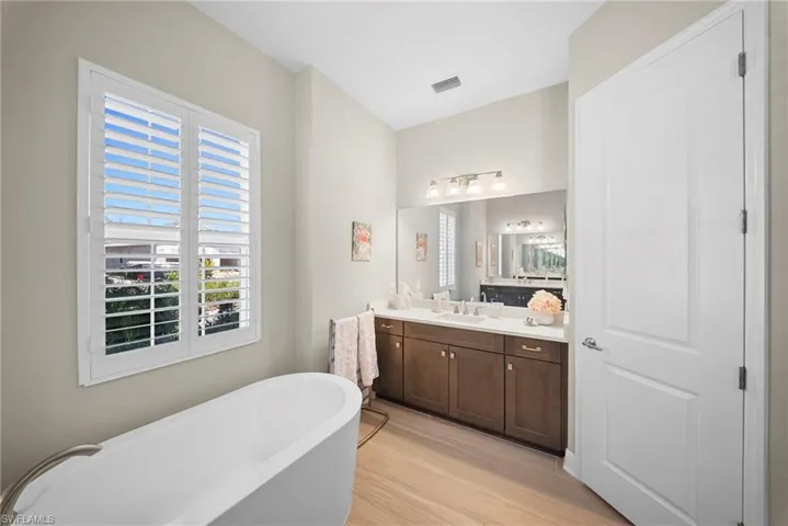The bathroom features a freestanding tub, a vanity with double sinks, and a large window with white plantation shutters