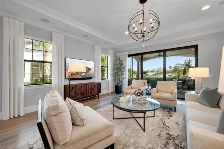 Living room with an inviting chandelier, crown molding, a tray ceiling, and light hardwood / wood-style flooring