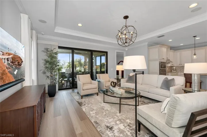 Living room with light hardwood / wood-style floors, crown molding, a tray ceiling, and a chandelier