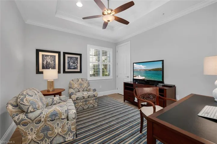 Office space featuring a raised ceiling, crown molding, ceiling fan, and wood-type flooring