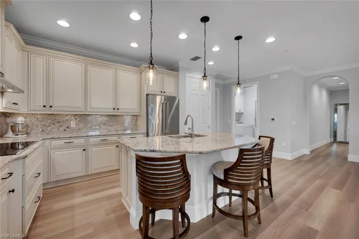 Kitchen featuring sink, light stone counters, light hardwood / wood-style floors, high end fridge, and a center island with sink