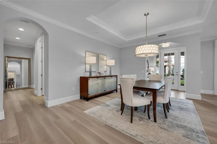 Dining area with a raised ceiling, french doors, light hardwood / wood-style floors, and ornamental molding