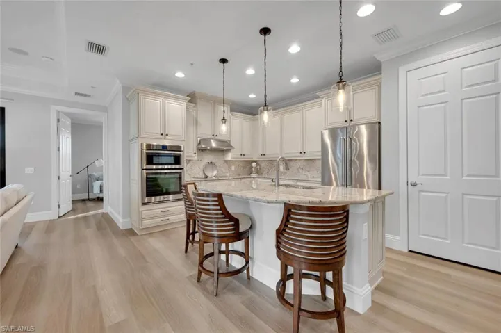 Kitchen featuring light stone countertops, stainless steel appliances, backsplash, pendant lighting, and a kitchen bar
