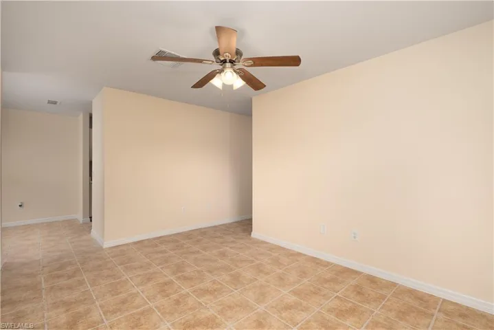 Spacious room featuring neutral wall tones, square tile flooring, white baseboards, a ceiling fan with integrated lighting, and recessed ceiling vents