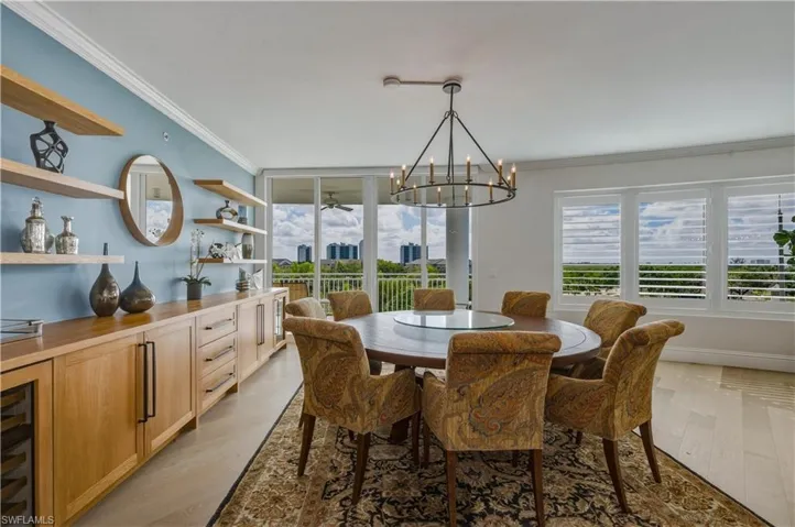 Dining area with a chandelier, crown molding, light wood-style floors, a ceiling fan, and wine cooler