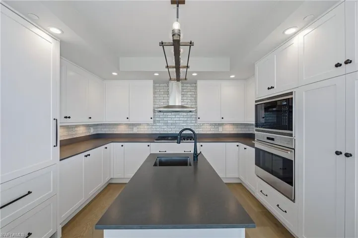 Kitchen featuring dark countertops, white cabinets, stainless steel appliances, decorative light fixtures, and a raised ceiling
