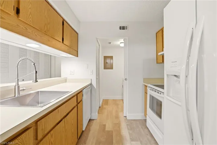 Kitchen with white appliances, light countertops, wood finish cabinetry, and light wood-style floors