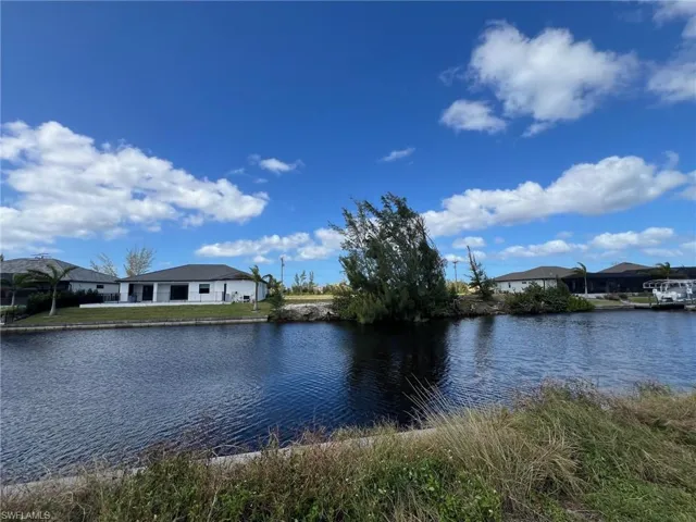 Canal-front property featuring a single-story residence with a dark roof and white exterior