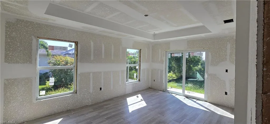Empty room with wood finished floors, a tray ceiling, and a wealth of natural light