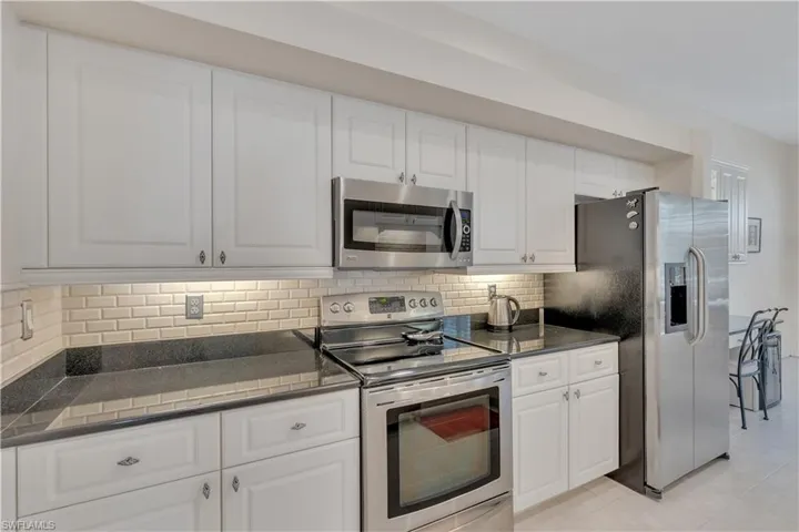 Kitchen featuring appliances with stainless steel finishes, dark countertops, tasteful backsplash, and white cabinets
