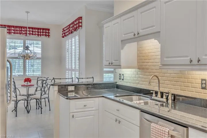 Kitchen with a sink, stainless steel dishwasher, white cabinetry, backsplash, and a peninsula