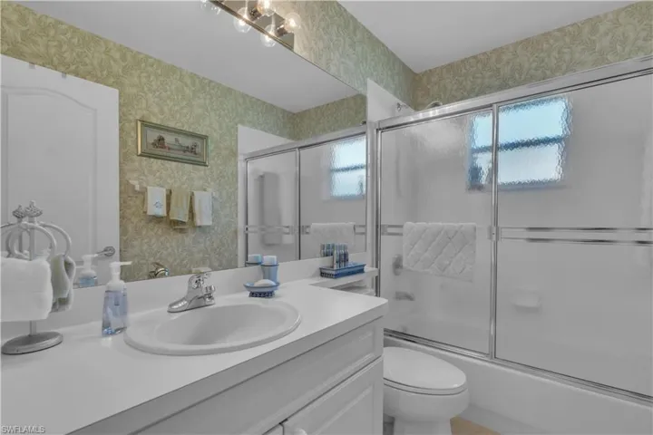 Full bath featuring wallpapered walls, vanity, shower / bath combination with glass door, and toilet