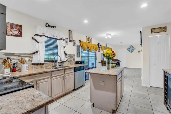Kitchen featuring decorative backsplash, light brown cabinetry, stainless steel dishwasher, a kitchen island, and sink