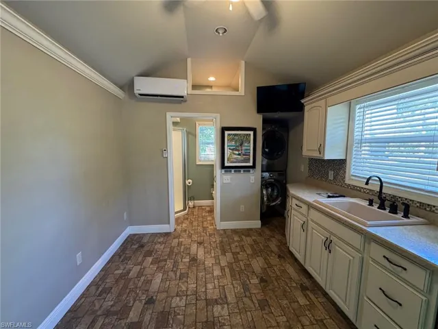 Kitchen with sink, a wall mounted air conditioner, plenty of natural light, decorative backsplash, and stacked washer and clothes dryer