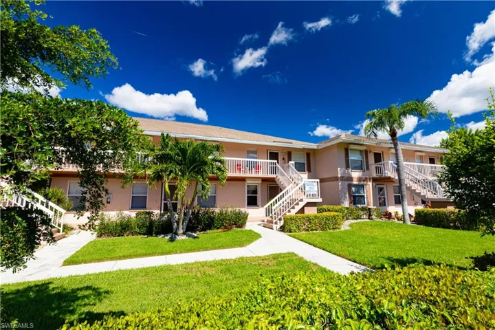 Two-story multi-unit building featuring a peach-toned exterior, multiple white outdoor staircases, and individual private balconies with white railings
