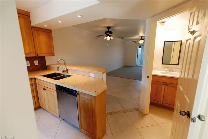 Kitchen featuring light wood cabinetry, a double basin stainless steel sink with a gooseneck faucet, light granite-finish countertops, and a full-size dishwasher