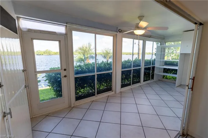 Sunroom featuring expansive water frontage, full-height windows, a ceiling fan, tiled flooring, and built-in shelving