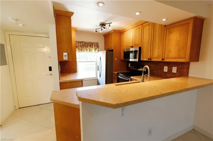 Kitchen featuring wood cabinetry, stainless steel appliances, speckled stone countertops, and a stone-finish backsplash