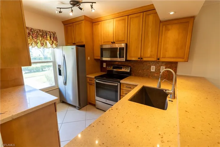 Kitchen featuring wood cabinetry, light-toned countertops, stainless steel appliances, and a tile backsplash