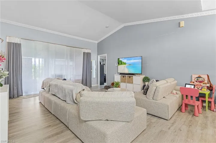 Living room featuring vaulted ceiling, ornamental molding, and light hardwood / wood-style flooring