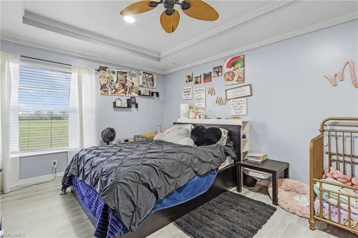 Bedroom featuring hardwood / wood-style floors, ceiling fan, a tray ceiling, and crown molding