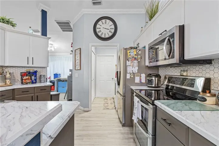 Kitchen with white cabinetry, ornamental molding, light wood-type flooring, stainless steel appliances, and tasteful backsplash