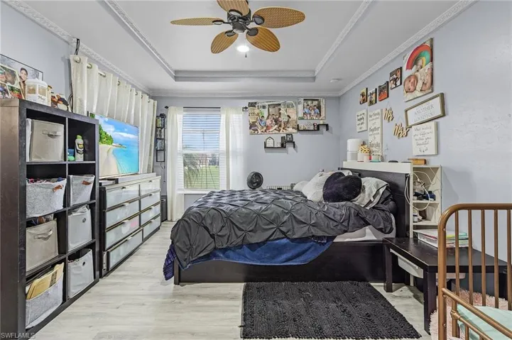 Bedroom featuring ceiling fan, ornamental molding, light hardwood / wood-style flooring, and a raised ceiling