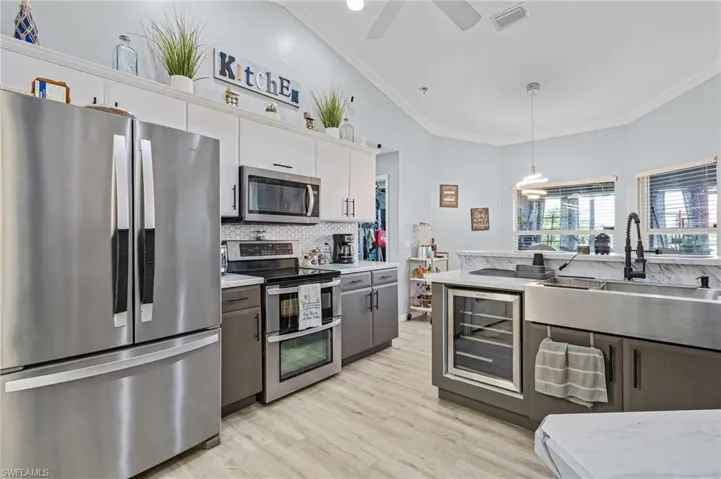 Kitchen featuring beverage cooler, light hardwood / wood-style floors, stainless steel appliances, hanging light fixtures, and white cabinetry