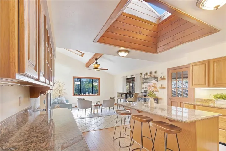 Kitchen featuring lofted ceiling with skylight, a kitchen breakfast bar, light stone countertops, ceiling fan, and light hardwood / wood-style flooring