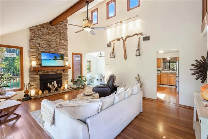 Living room featuring a fireplace, ceiling fan, wood-type flooring, and high vaulted ceiling