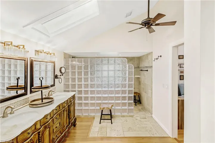 Bathroom featuring wood-type flooring, tiled shower, vanity, vaulted ceiling, and ceiling fan