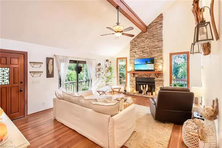 Living room featuring a stone fireplace, beam ceiling, high vaulted ceiling, hardwood / wood-style flooring, and ceiling fan