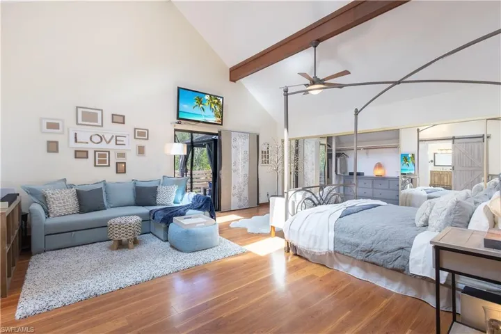 Bedroom with a barn door, beam ceiling, light hardwood / wood-style flooring, and high vaulted ceiling