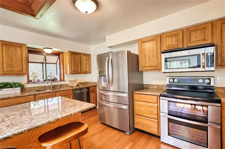 Kitchen with light wood-type flooring, appliances with stainless steel finishes, sink, and light stone countertops