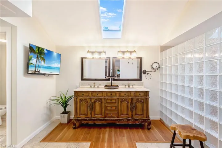 Bathroom featuring hardwood / wood-style floors, vanity, toilet, and vaulted ceiling with skylight