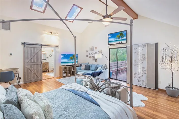 Living room featuring ceiling fan, a barn door, light hardwood / wood-style floors, and beamed ceiling