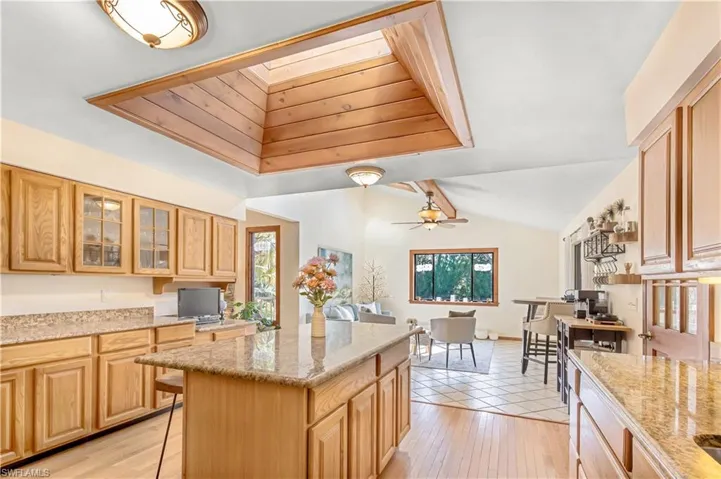 Kitchen featuring a kitchen island, vaulted ceiling, light stone counters, and light hardwood / wood-style flooring